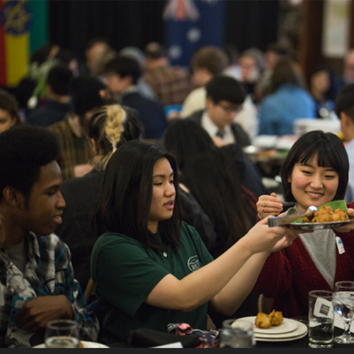 Students pass a plate of food at a dinner event