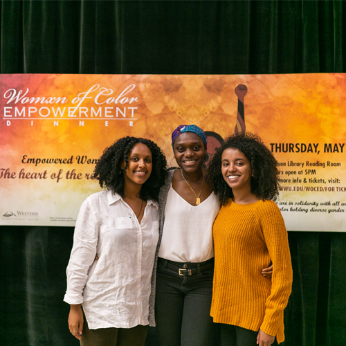 Three people smiling at the camera with women of color empowerment banner in the background